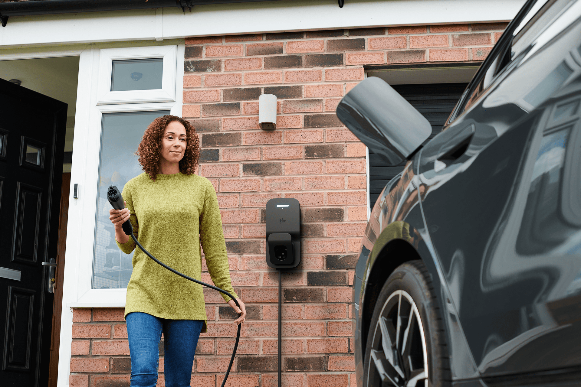 Flo Home Black X3 EV charging station, installed outside of home, woman charging an EV car