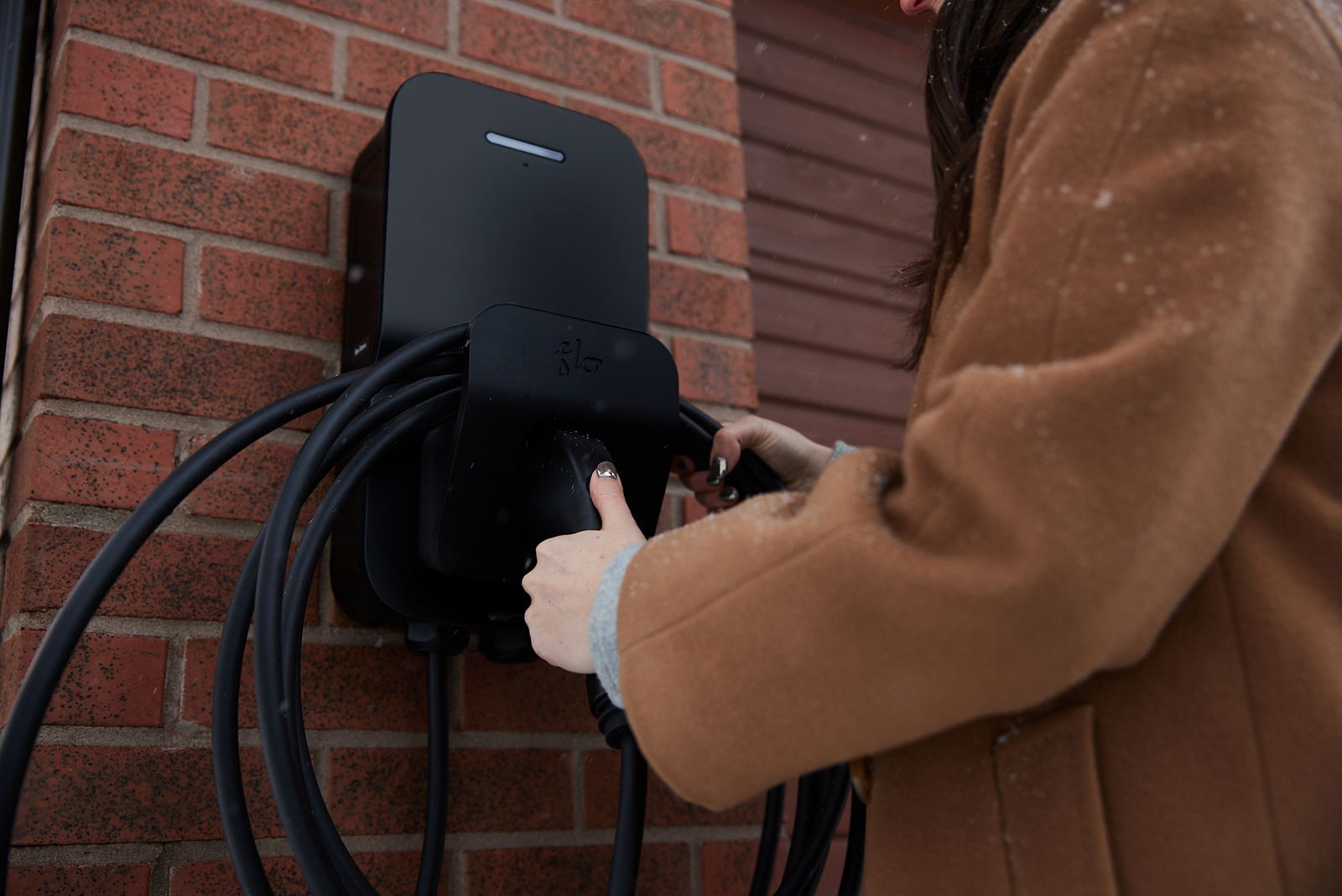 Black FLO Home X6 EV charger installed on the exterior wall of a home in winter side view 