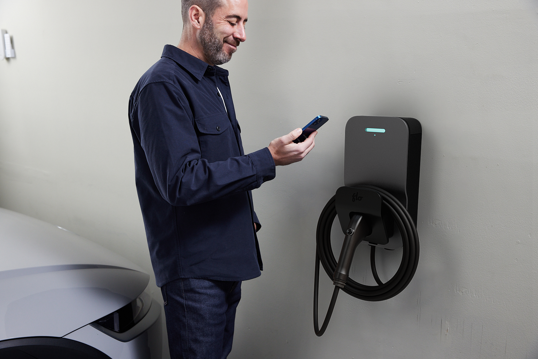 User checking the mobile app next to a black FLO Home X6 charger indoors