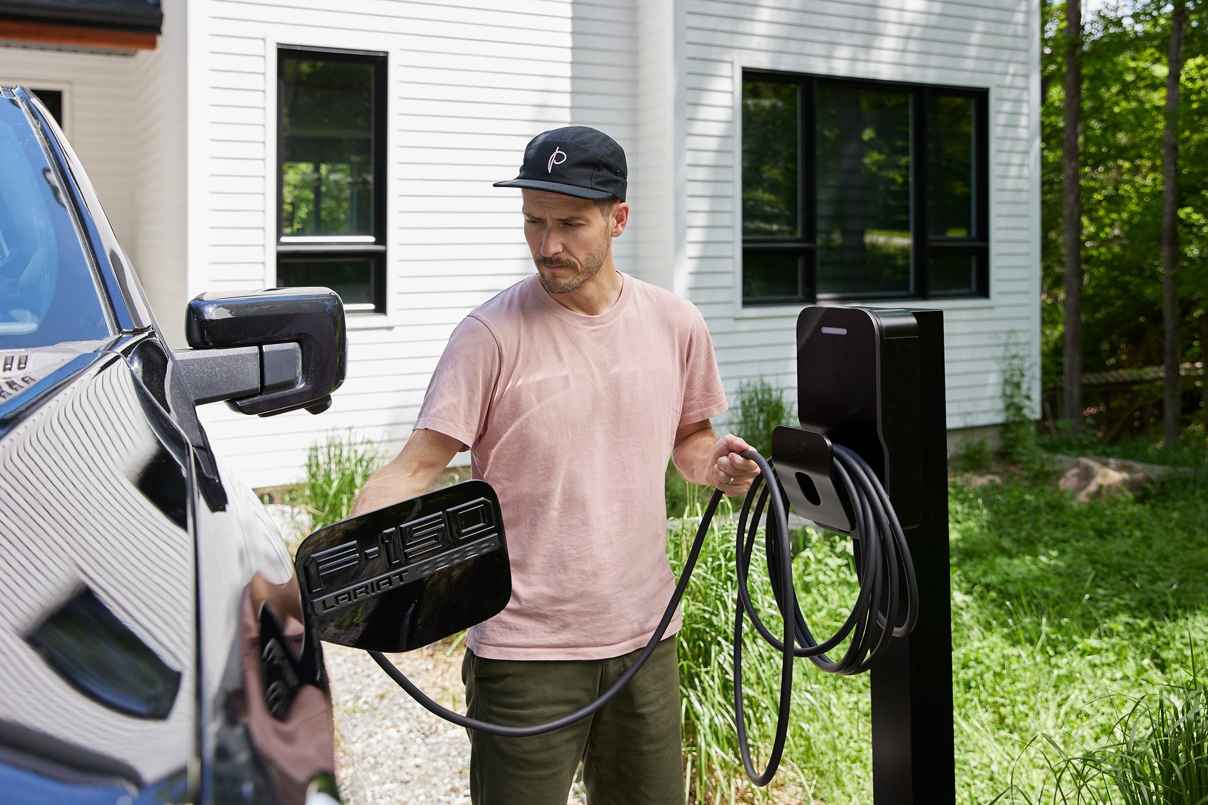 Flo Home, a photo off the black basic pedestal installed outside off a home while a men charges his EV truck 