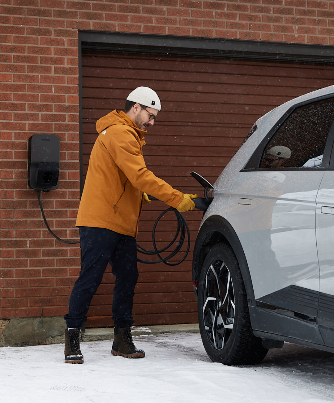 Black FLO Home X3 EV charger installed on the exterior wall of a house home while a man charges his grey EV in winter