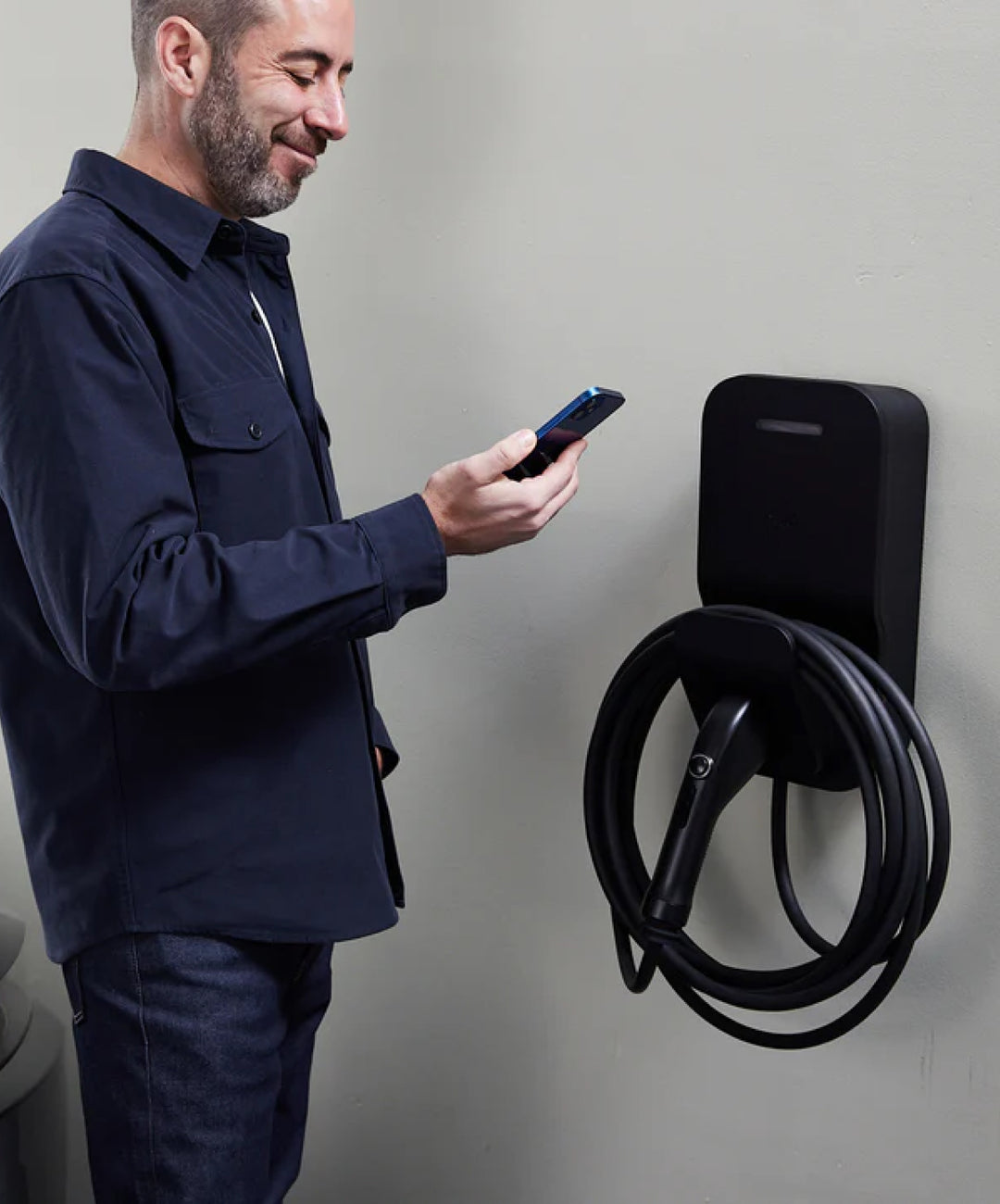 User checking the mobile app next to a black FLO Maison X3 charger indoors