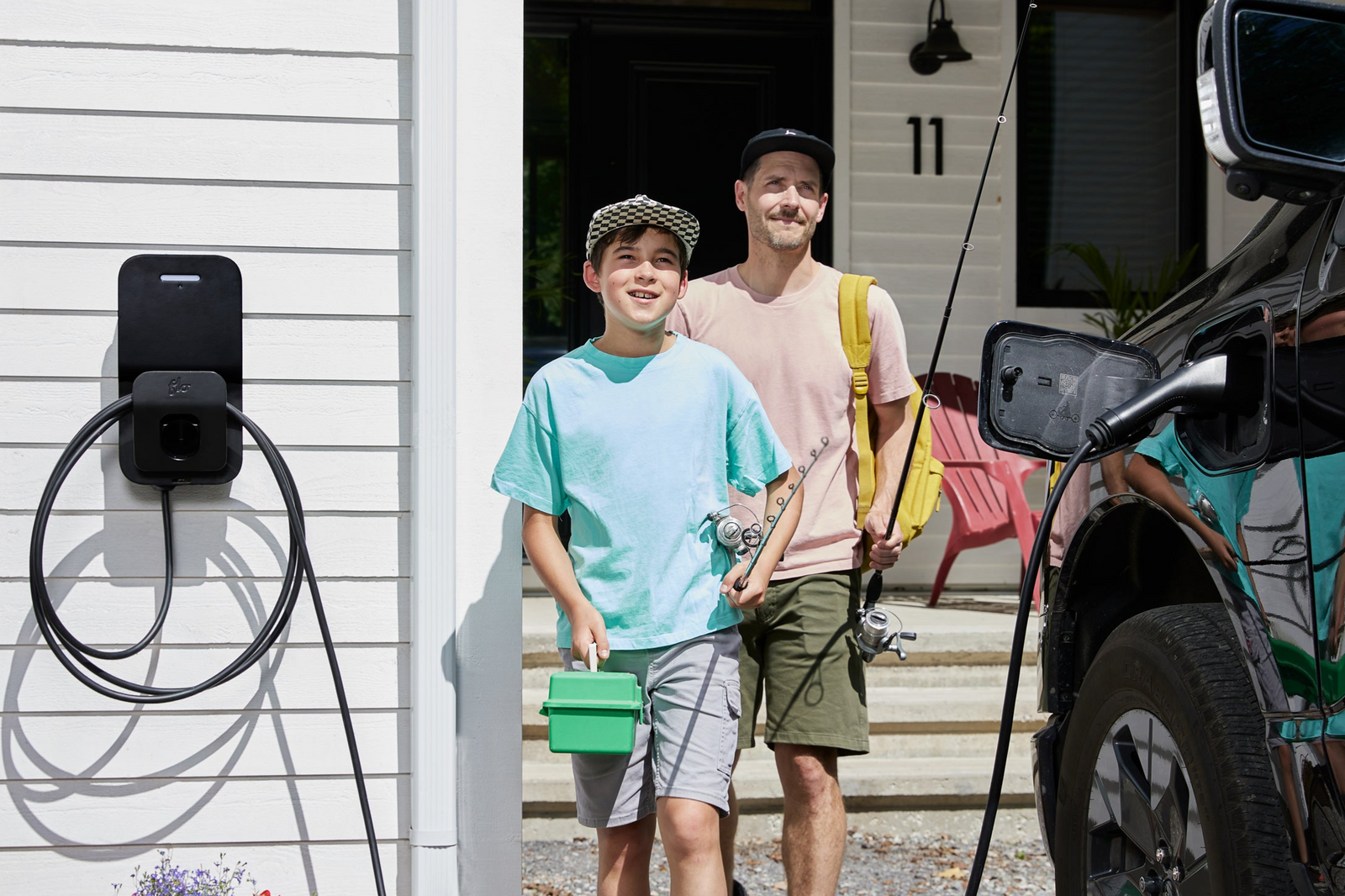 Two people standing outside a house with a  Flo Home X8 electric vehicle charging station in summer time